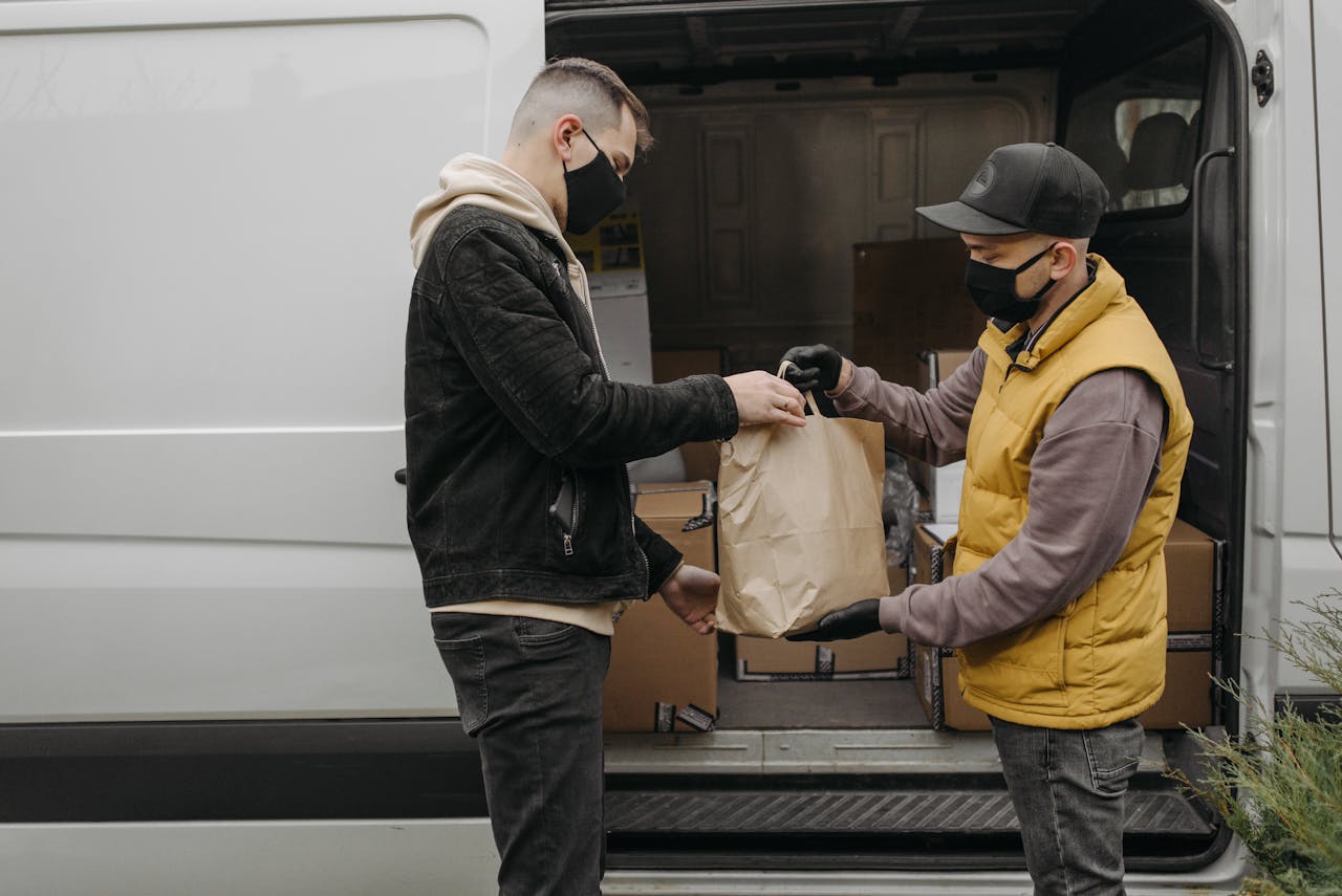 Masked deliveryman hands package to customer from van, ensuring safety and hygiene.